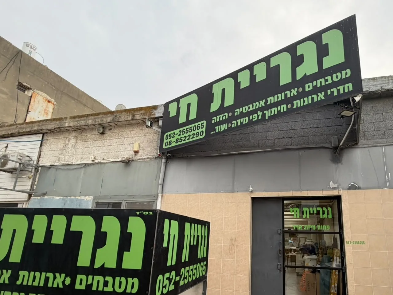 חזית נגריית חי ברחוב העבודה 40 באשדוד: שלט שחור-ירוק, דלת הזכוכית של התצוגה ועגלה ממותגת